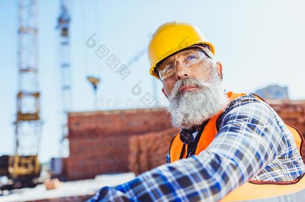 有胡须的工人采用反射的马甲和建筑工人sitt采用g在建设