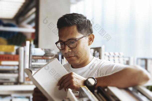 年幼的男人阅读书采用一书商店.