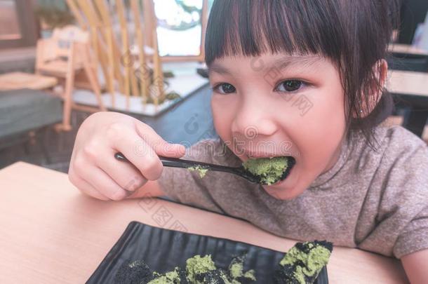 小的小孩幸福的吃绿色的茶水日本抹茶蛋糕辗