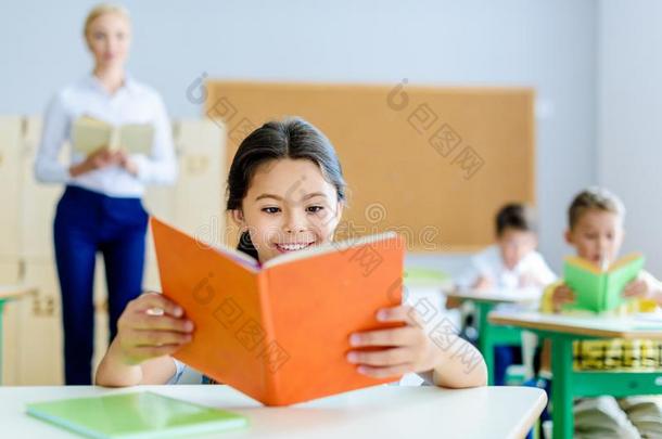 美丽的微笑的女学生阅读书在教室