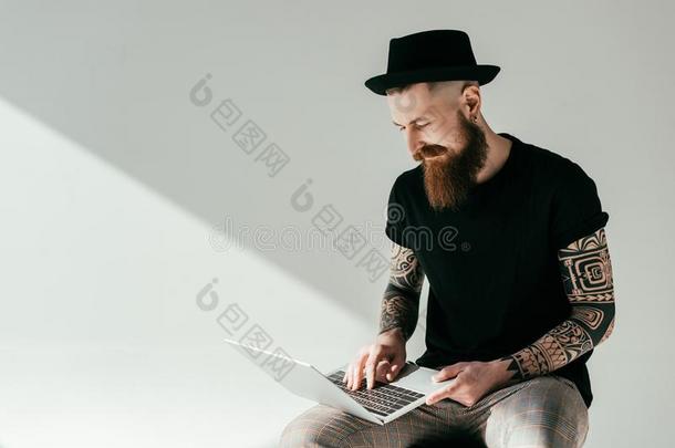 英俊的有胡须的<strong>刺青</strong>男人有样子的在便携式电脑