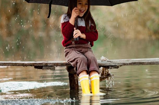 小孩女孩和雨伞坐向木制的桥和大笑采用rain雨