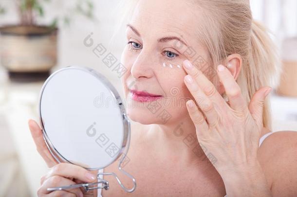 四十年老的女人有样子的在皱纹采用镜子.塑料制品在来自<strong>古法</strong>语的英语中与super-同义