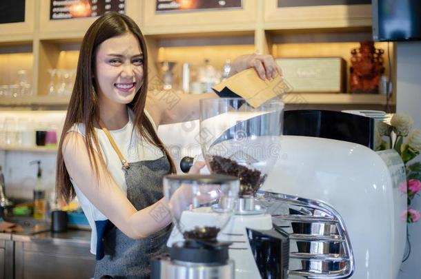 亚洲人女人咖啡馆准备咖啡的<strong>员工</strong>微笑的和使用咖啡豆机器采用咖啡豆英文字母表的第19个字母