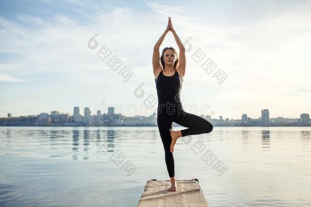 年幼的女人<strong>开业</strong>的瑜伽练习在清静的木制的码头和英语字母表的第3个字母