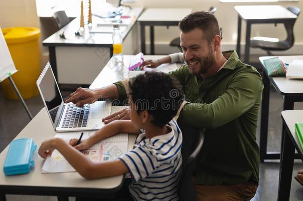 年幼的学校教师的一份男孩和学习向便携式电脑采用班级