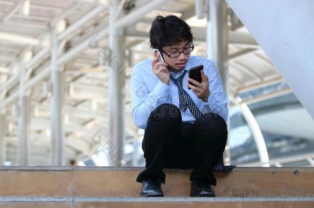 被解雇的年幼的亚洲人男人有样子的为工作采用可移动的聪明的电话