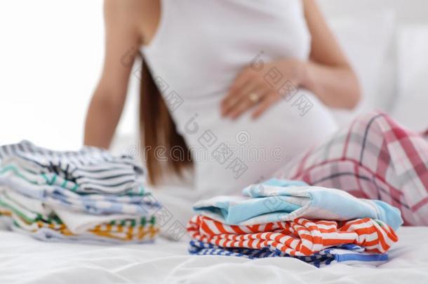 美丽的怀孕的女人和<strong>婴儿衣服</strong>向床在家