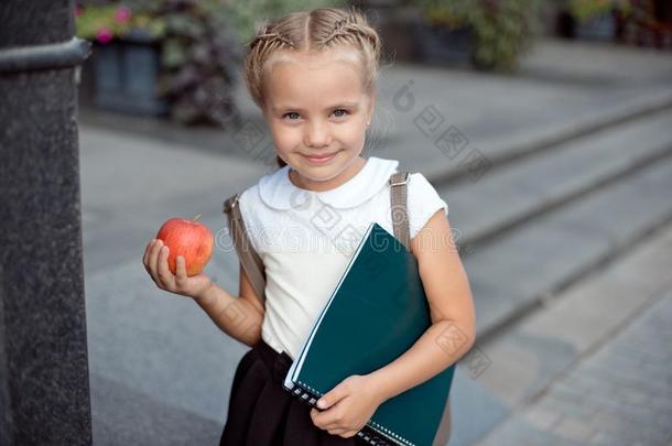 幸福的小的女学生和亚麻色的头发采用学校制服和英语字母表的第12个字母