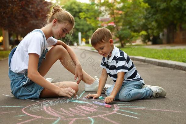 青少年保姆和漂亮的小的男孩绘画太阳和制造白色或彩色粉笔的白垩