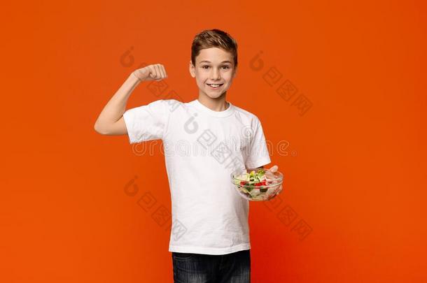 强的十几岁的青少年和新鲜的蔬菜沙拉展映他的肌肉
