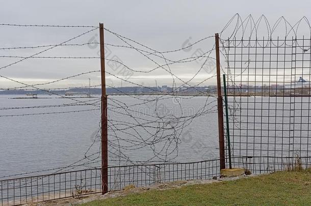 栅栏和装有倒钩的金属丝,和海和海岸采用指已提到的人背景