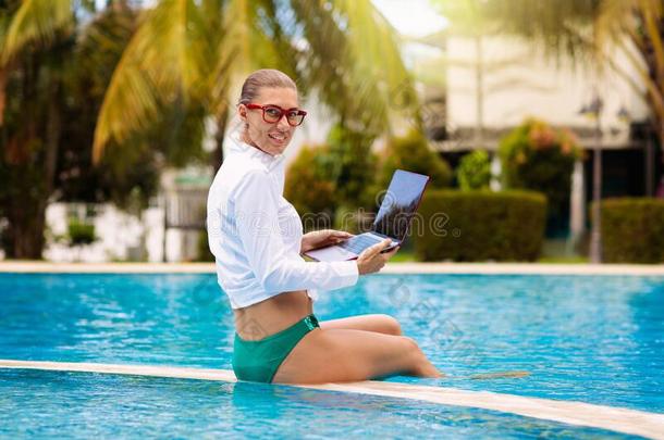 女人和便携式电脑在游泳水池.遥远的使工作