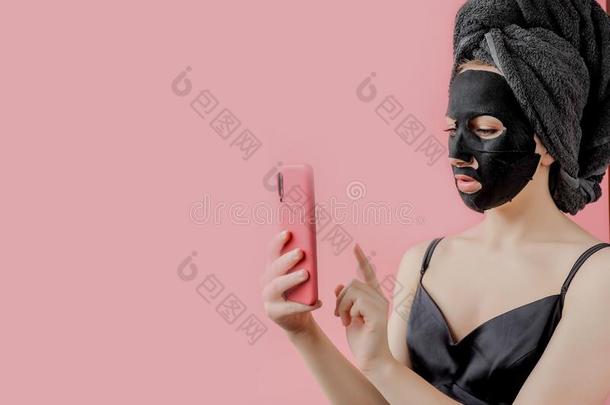 年幼的女人应用黑的化妆品织物面部的面具和电话采用