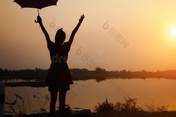轮廓关于女儿增加一雨伞向天在日落在旁边湖