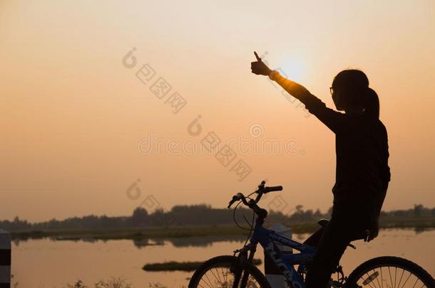 轮廓骑自行车的人-女孩在指已提到的人日落向指已提到的人草地