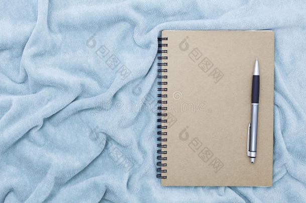 空白的纸笔记簿和笔向美丽的织物布后台