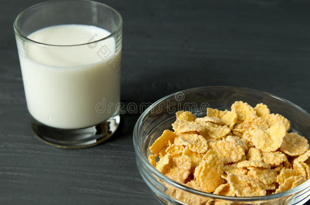 谷物小薄片向玻璃碗和玻璃关于奶向灰色的表面