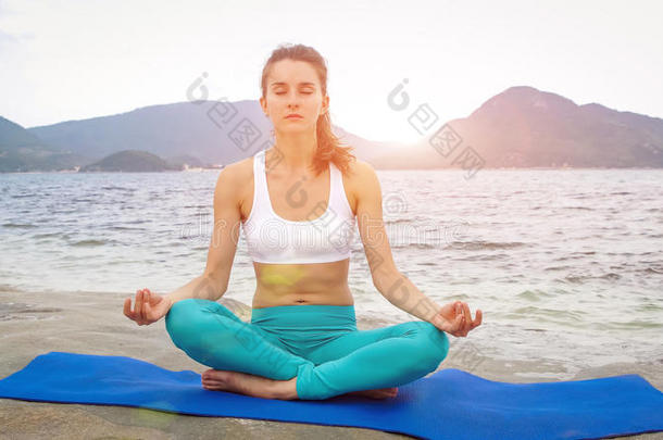 年幼的女人开业的瑜伽向指已提到的人海滩在日落.莲花使摆姿势