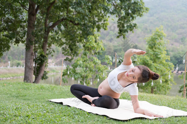 亚洲人怀孕的女人开业的瑜伽向绿色的草采用公众的爸