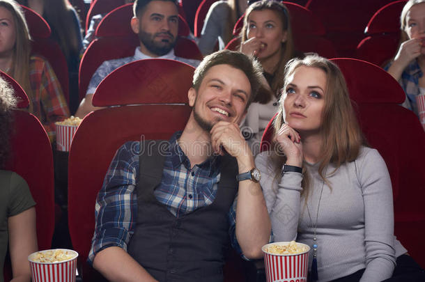 严肃的女人和微笑的男人观察电影在现代的电影院.