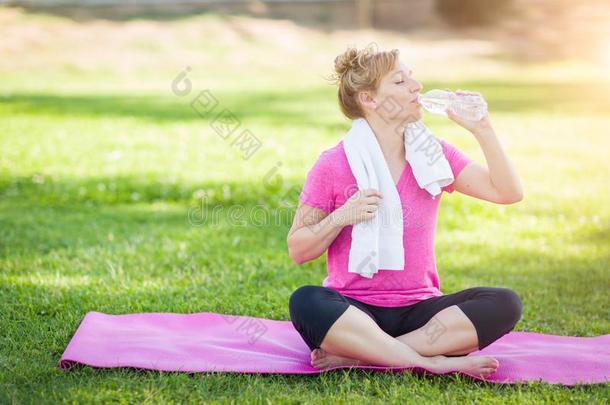 运动员的成熟的女人在户外向瑜伽席子所有水