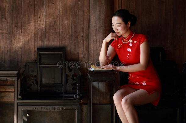 幸福的中国人女人采用红色的旗袍阅读书