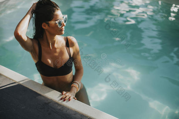 漂亮的年幼的女人放松心情向指已提到的人游泳池边
