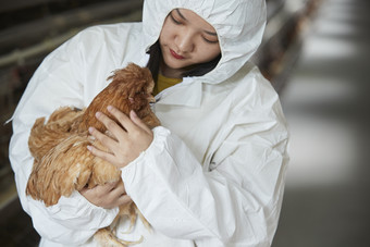 身穿防护服怀抱家禽的年轻女性饲养员