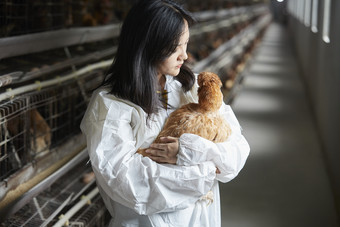 身穿防护服怀抱家禽的年轻女性饲养员