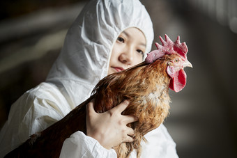 身穿防护服怀抱家禽的年轻女性饲养员