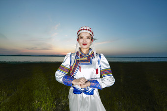 晚霞的草原湖畔穿蒙古族传统服饰的年轻女性