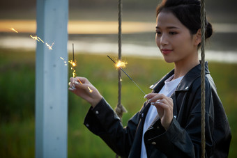 夕阳下湖畔秋千上燃放仙女棒的可爱少女