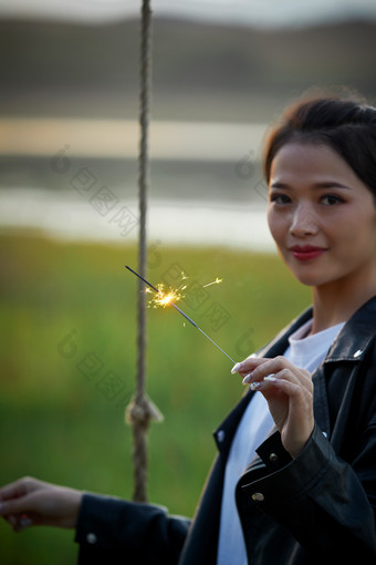 夕阳下湖畔秋千上燃<strong>放</strong>仙女棒的可爱少女