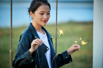 夕阳下湖畔秋千上燃放仙女棒的可爱少女