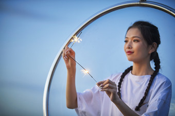 傍晚湖畔透明秋千上燃<strong>放</strong>仙女棒的可爱少女