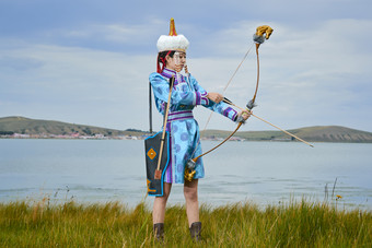 草原湖畔身穿蒙古族饰手持弓箭的蒙族少女
