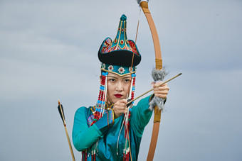 草原湖畔身穿蒙古族饰手持弓箭的蒙族少女