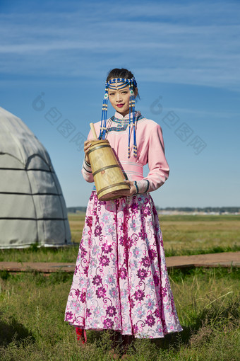 蒙古包前穿蒙古族饰怀抱奶茶桶的蒙族少女