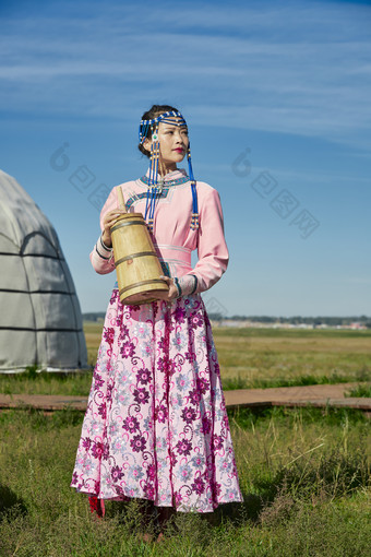 蒙古包前穿蒙古族饰怀抱奶茶桶的蒙族少女