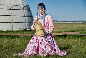 蒙古包前穿蒙古族饰怀抱奶茶桶的蒙族少女