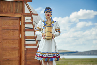 蒙古包前穿<strong>蒙古族</strong>饰怀抱奶茶桶的蒙族少女