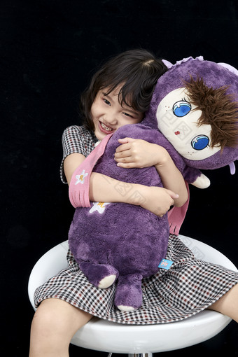 黑色背景里坐在凳子上抱着娃娃玩耍的可爱亚洲小女孩儿童