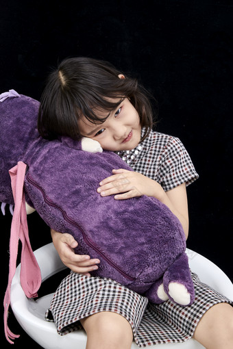 黑色背景里坐在凳子上抱着娃娃玩耍的可爱亚洲小女孩儿童