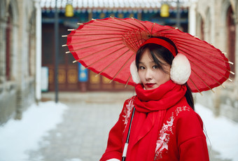 雪后在老城古巷穿着喜庆服饰的亚洲少女