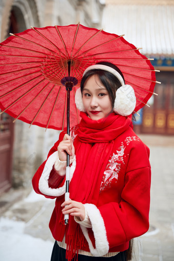 雪后在老城古巷穿着喜庆服饰的亚洲少女