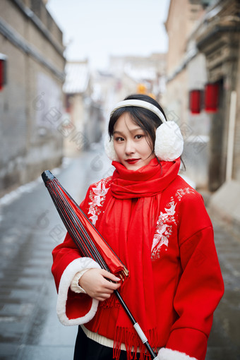 雪后在老城古巷穿着喜庆服饰的亚洲少女