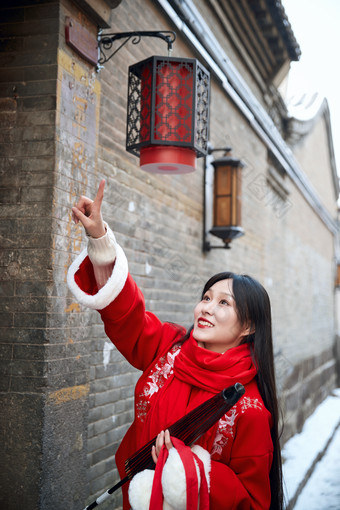 雪后在老城古巷穿着喜庆服饰的亚洲少女