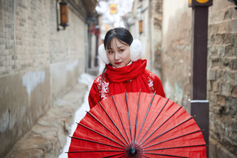 雪后在老城古巷穿着喜庆服饰的亚洲少女