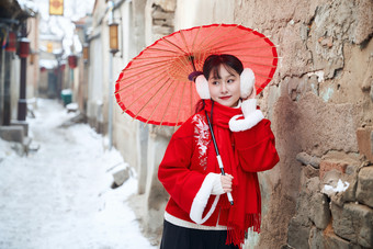 雪后在老城古巷穿着喜庆服饰的亚洲少女